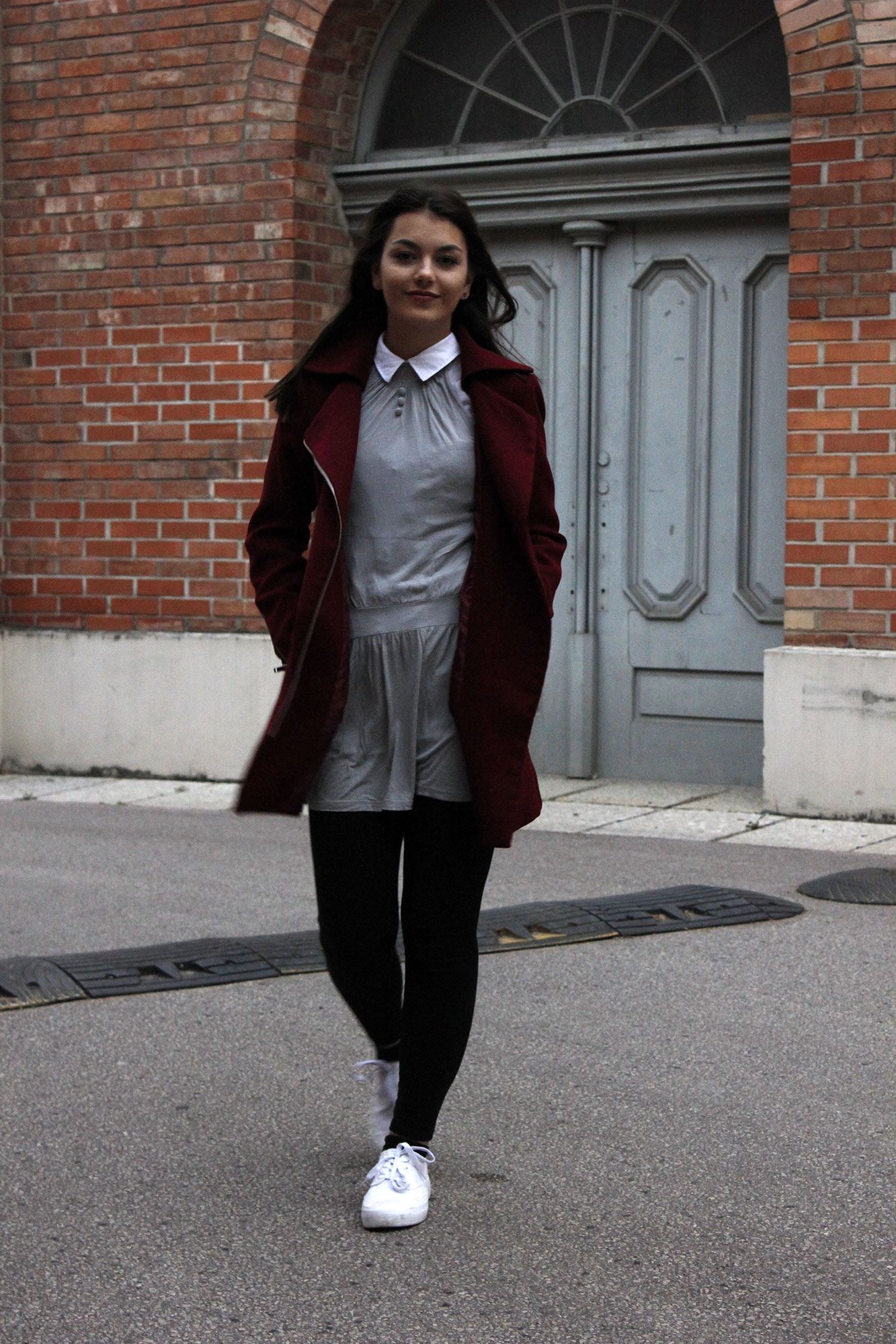 Dorie walking, wearing a red coat, grey dress, black legging and white shoes